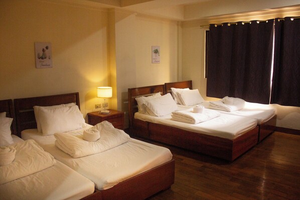 Una habitación de hotel con dos camas, una mesita de noche con lámpara y una ventana con cortinas.