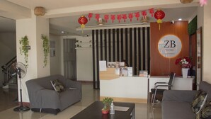 A hotel reception area with a reception desk, two sofas, a coffee table, and a staircase.