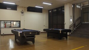 A room with two pool tables, a staircase, and a large window.