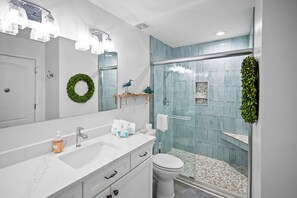 A bathroom with a white vanity, a glass shower enclosure, and a green wreath on the wall. - Indies 406 | 1BR/1BA Gulf-View Condo | Sleeps 4 | Balcony & Pool Access (GULF SHORES)