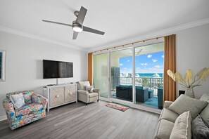 A living room with a sofa, armchair, TV, and a balcony with a view. - Indies 406 | 1BR/1BA Gulf-View Condo | Sleeps 4 | Balcony & Pool Access (GULF SHORES)