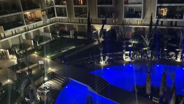 Een hotel met meerdere verdiepingen, een zwembad, terras en palmbomen.