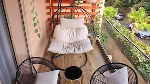 Een balkon met een hangstoel, twee bijzetzels, een klein rond tafeltje en een houten wand met planten.