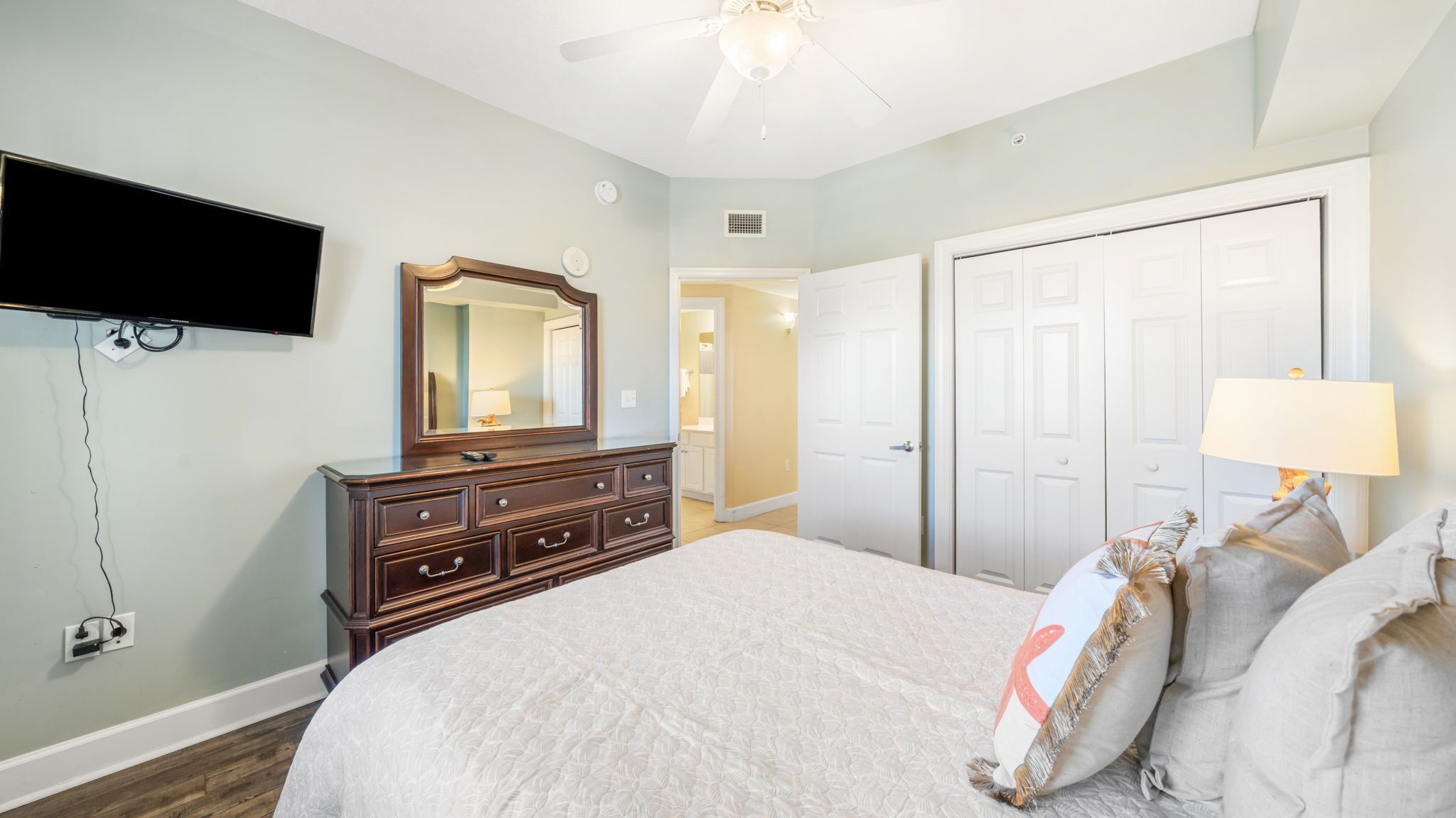 A bedroom with a bed, dresser, mirror, TV, and closet.