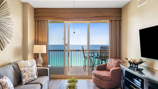 A room with a sofa, armchair, TV, and a balcony with a view of the ocean. - Gulf-Front Sunrise Beach Resort | Family Favorite | Sleeps 8 | Near Pier Park (Panama City Beach)