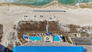 An aerial view of a beach resort with a swimming pool, sun loungers, and a large blue building. - Gulf-Front Sunrise Beach Resort | Family Favorite | Sleeps 8 | Near Pier Park (Panama City Beach)