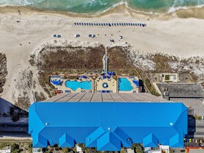 Eine Vogelperspektive auf ein Strandresort mit Schwimmbad, Liegestühlen und einem großen, blauen Gebäude.