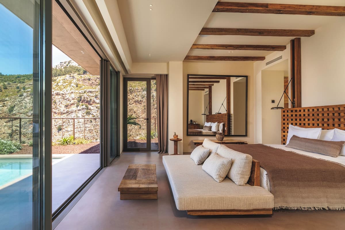 A bedroom with a large bed, a sofa, a wooden coffee table, and a view of a pool and outdoor area.