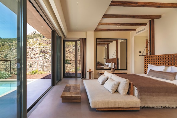 Ein Schlafzimmer mit einem großen Bett, einer Schlafcouch, einem Holztisch und Blick auf einen Pool und Außenbereich.