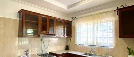 Une cuisine avec des meubles de rangement en bois, une cuisinière, un évier et une fenêtre avec des rideaux.