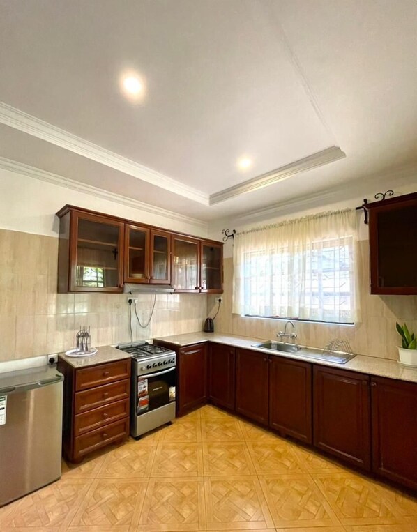 Une cuisine avec des meubles de rangement en bois, une cuisinière, un évier et une fenêtre avec des rideaux.