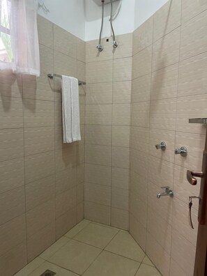 Une douche d’angle avec des carreaux de couleur beige, une serviette blanche et un pommeau de douche.