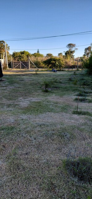 A grassy field with a wooden gate, trees, and a clear sky. - Modern Eco-Container Retreat: 2 Blocks from the Ocean, 1-bedroom house with AC. (Ba Buenos Aires ,Maldonado)
