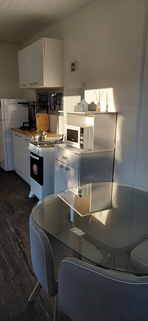A compact kitchen with a gas stove, microwave, refrigerator, and a glass dining table. - Modern Eco-Container Retreat: 2 Blocks from the Ocean, 1-bedroom house with AC. (Ba Buenos Aires ,Maldonado)