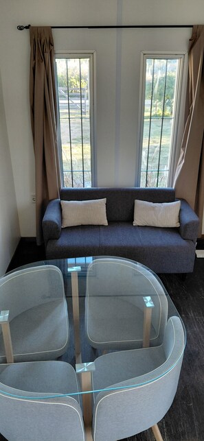A room with a grey sofa, two windows with curtains, and a glass table with chairs. - Modern Eco-Container Retreat: 2 Blocks from the Ocean, 1-bedroom house with AC. (Ba Buenos Aires ,Maldonado)