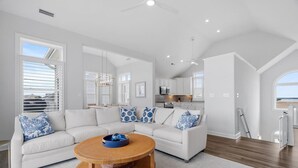 A modern living room with a sectional sofa, a round coffee table, and a kitchen area in the background. - New / Oceanview / Heated Pool • Steps to Beach (Virginia Beach)