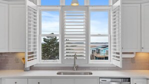 A kitchen with a large window, white cabinets, a stainless steel sink, and a dishwasher. - New / Oceanview / Heated Pool • Steps to Beach (Virginia Beach)