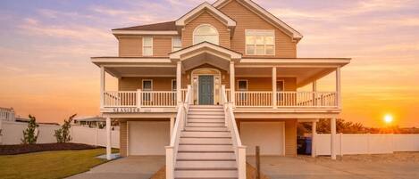 A two-story house with a front porch, a staircase leading to the entrance, and a clear sky.