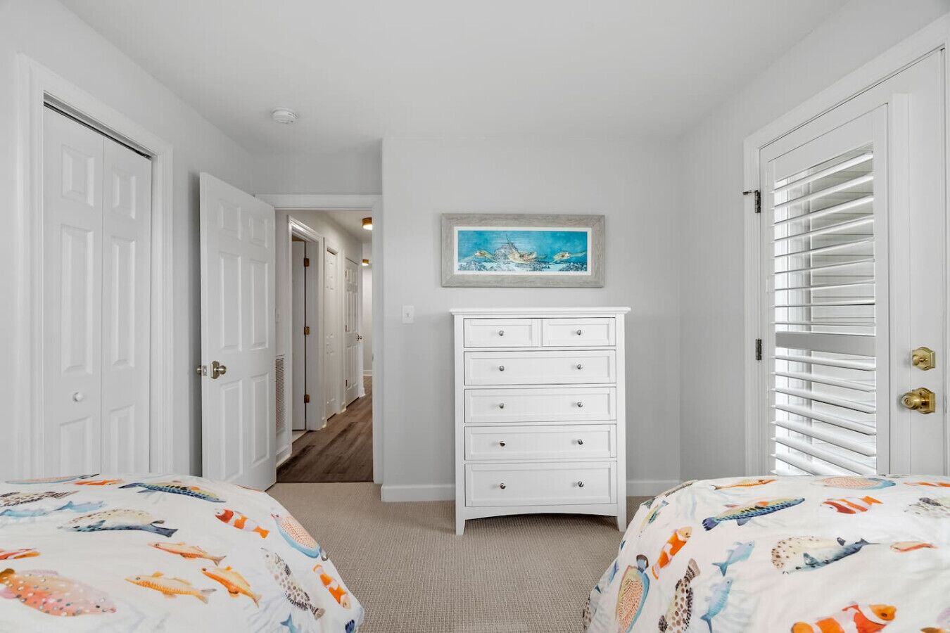 A bedroom with two beds, a dresser, a painting, and a hallway leading to another room.
