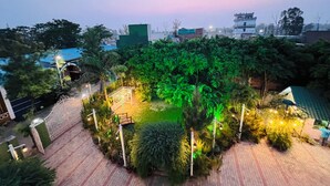 A courtyard with a paved walkway, surrounded by lush greenery and trees, with a building in the background. - Hotel Green Garden in Ludhiana, Couple friendly Near Railway Station (Ludhiana)