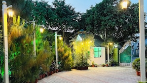 A paved pathway leading to a small structure with a green roof, surrounded by various potted plants and trees. - Hotel Green Garden in Ludhiana, Couple friendly Near Railway Station (Ludhiana)