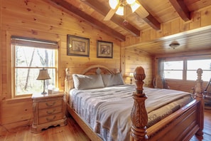 A wooden cabin bedroom with a bed, nightstand, lamp, and framed pictures on the wall. - Spacious Log Cabin w/ Stunning Views in Blue Ridge (Blue Ridge)