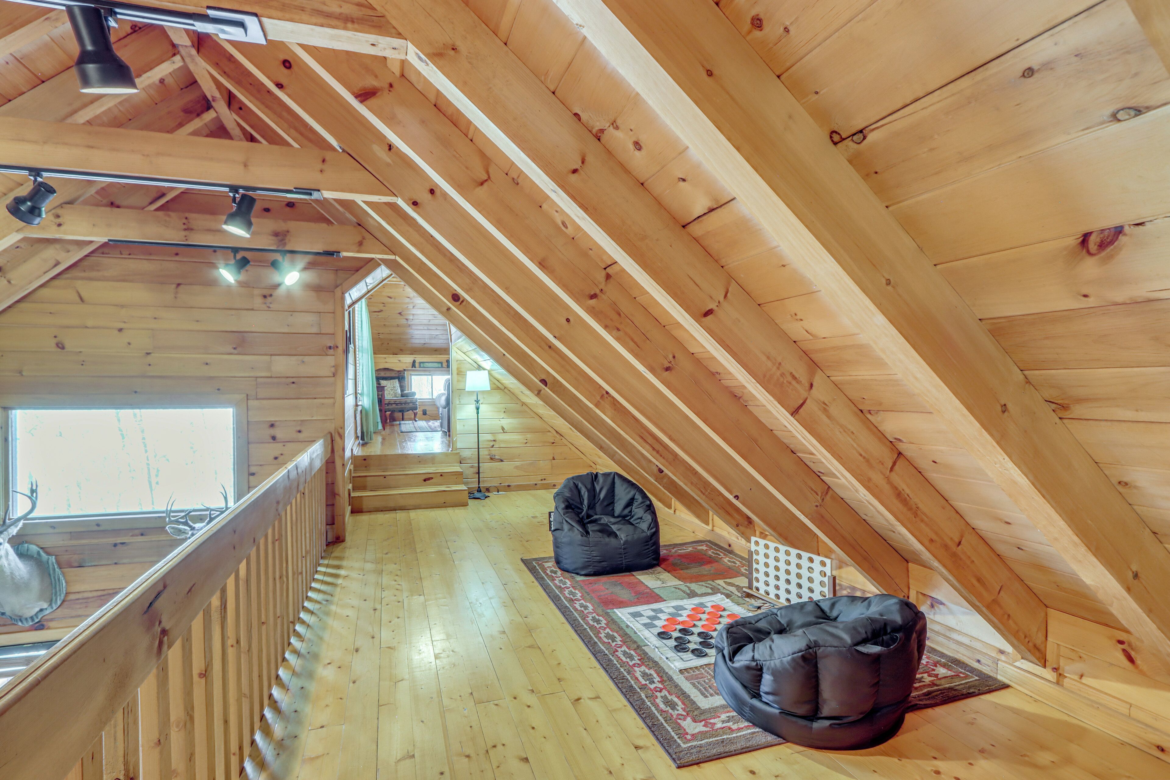 A wooden interior with a sloped ceiling, a window with a deer head decoration, a chessboard, and two bean bags.