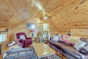 A cozy log cabin interior with a plush red armchair, a brown leather sofa, a wooden coffee table, and a ceiling fan. - Spacious Log Cabin w/ Stunning Views in Blue Ridge (Blue Ridge)