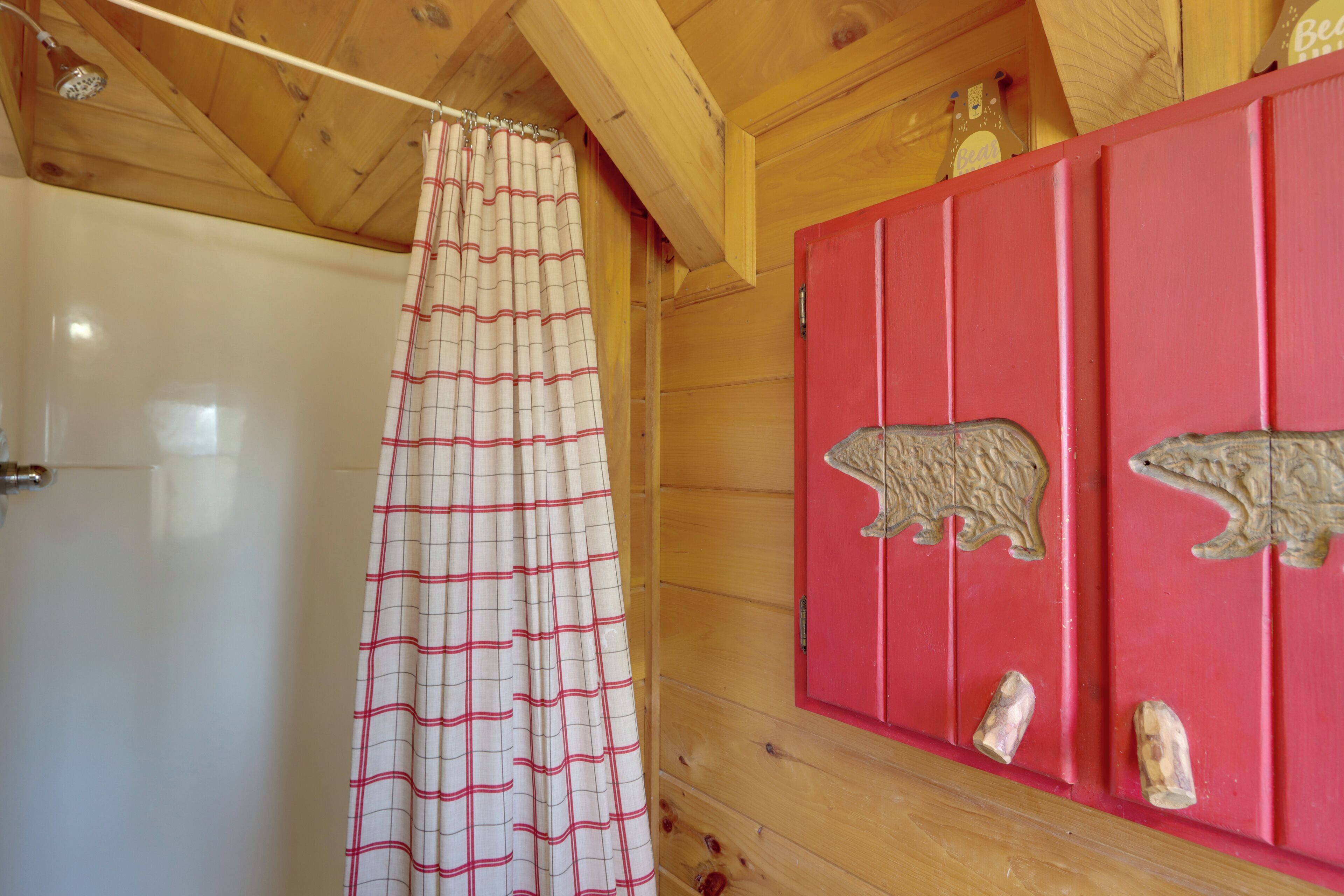 A wooden cabin interior with a shower curtain, a red cabinet with bear carvings, and wooden walls.