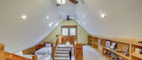 Ein Zimmer mit schrägem Dach, einer Holztreppe, zwei Betten, einem Schreibtisch und einem Bücherregal.