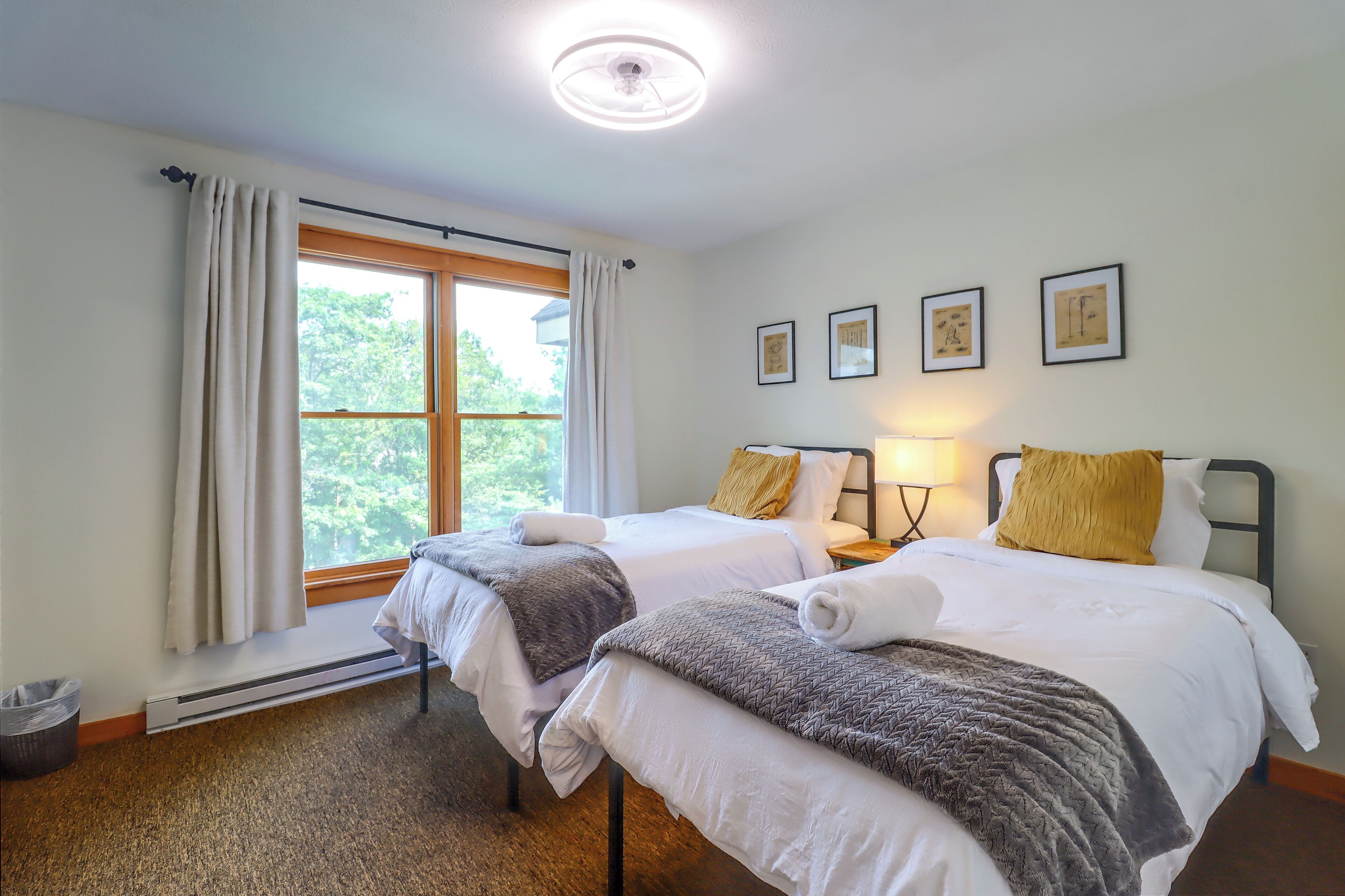 Ett hotellrum med två sängar, ett fönster med gardiner, ett element och inramade konstverk på väggen.