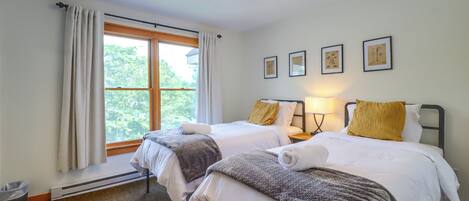 Ett hotellrum med två sängar, ett fönster med gardiner, ett element och inramade konstverk på väggen.
