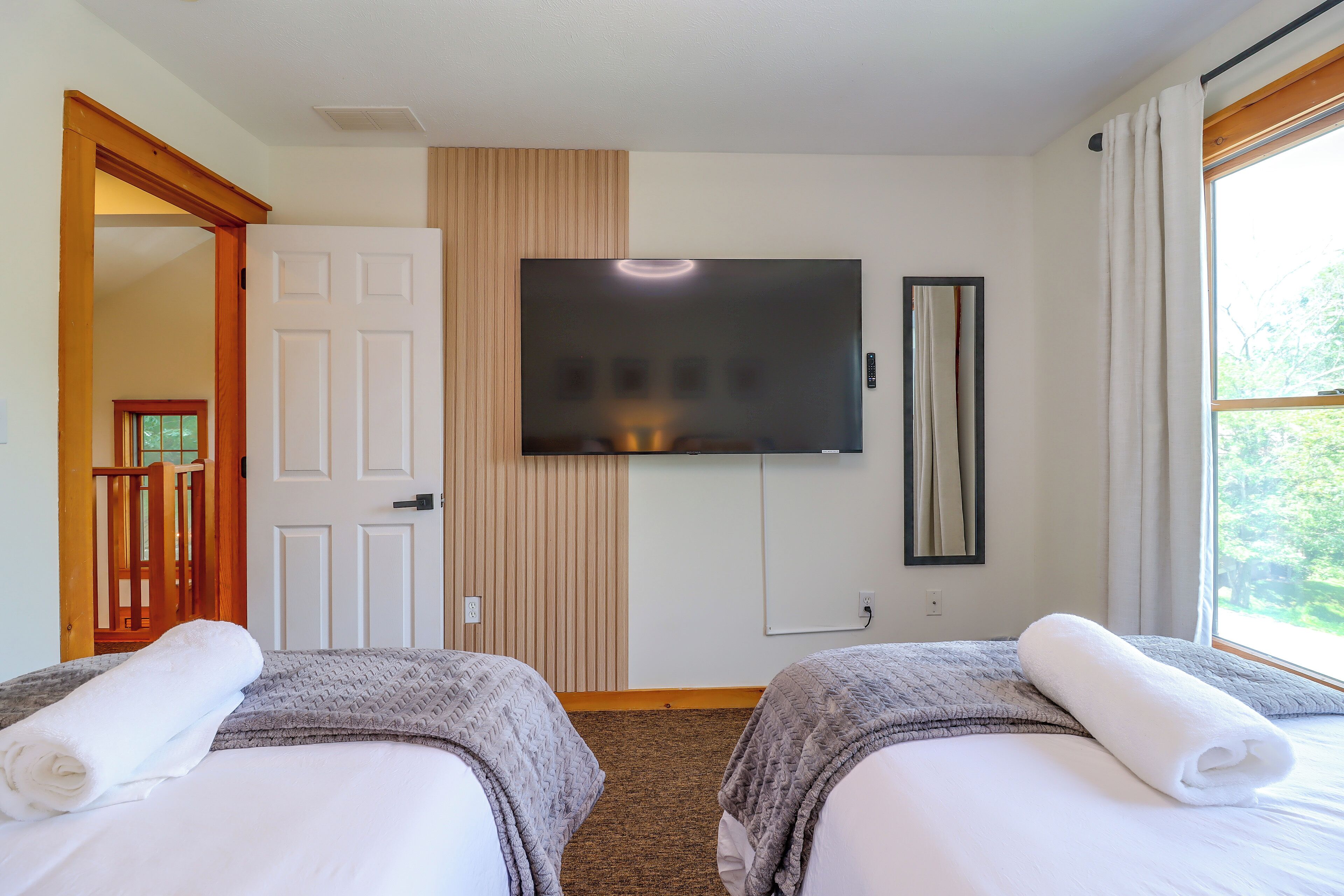 Ett hotellrum med två sängar, en TV, en spegel och ett fönster med gardiner.