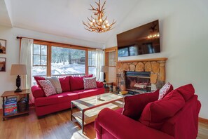 A living room with a red sofa, a wooden coffee table, a fireplace, and a large window with a view of a snowy landscape.