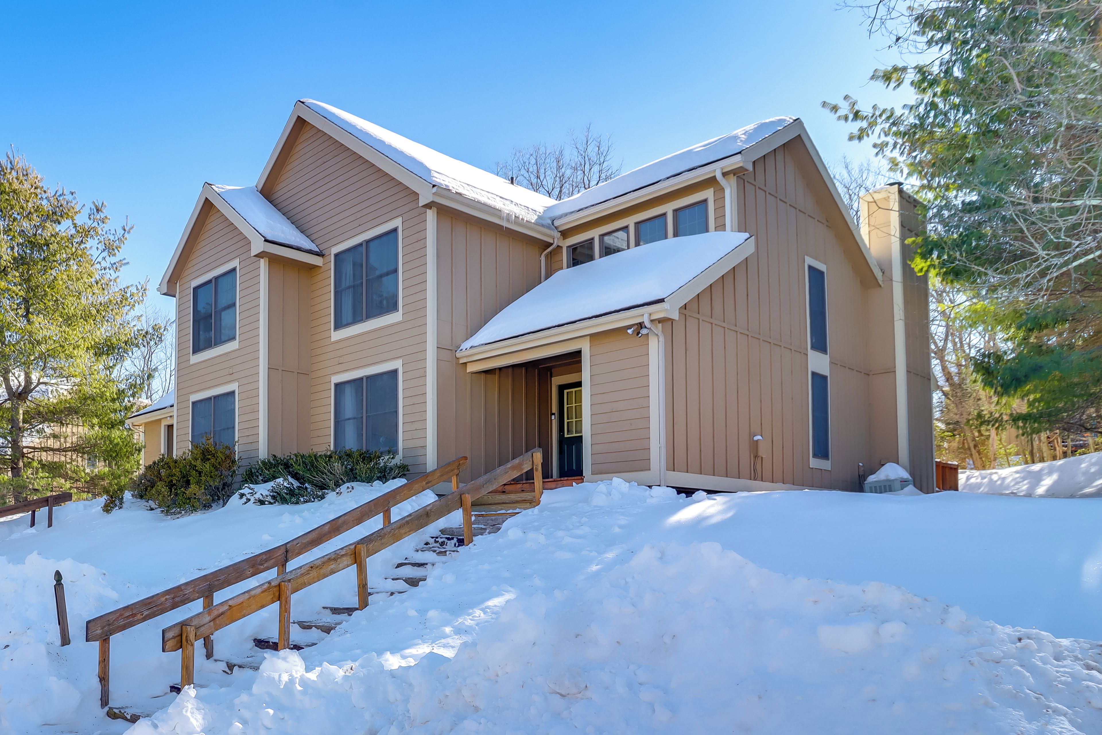 Une maison à deux étages, dont le toit est recouvert de neige, et un escalier en bois qui mène à l’entrée.