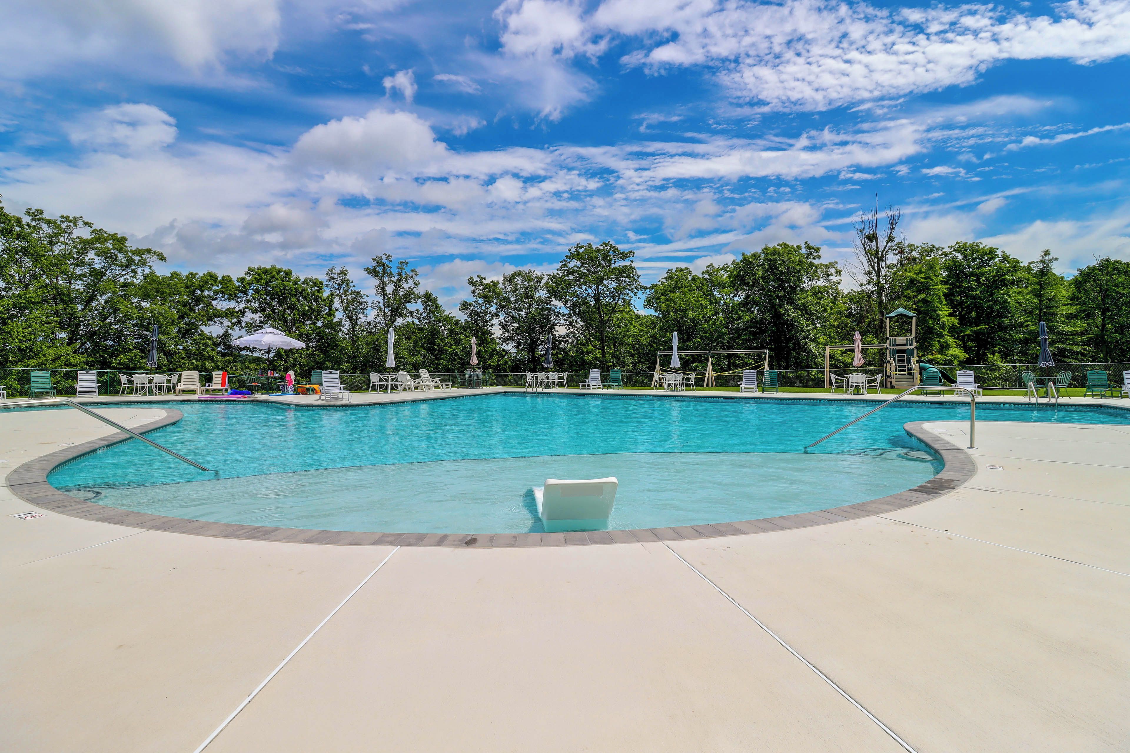 Une piscine à bordures courbes, entourée de chaises longues et de parasols, sous un ciel dégagé.