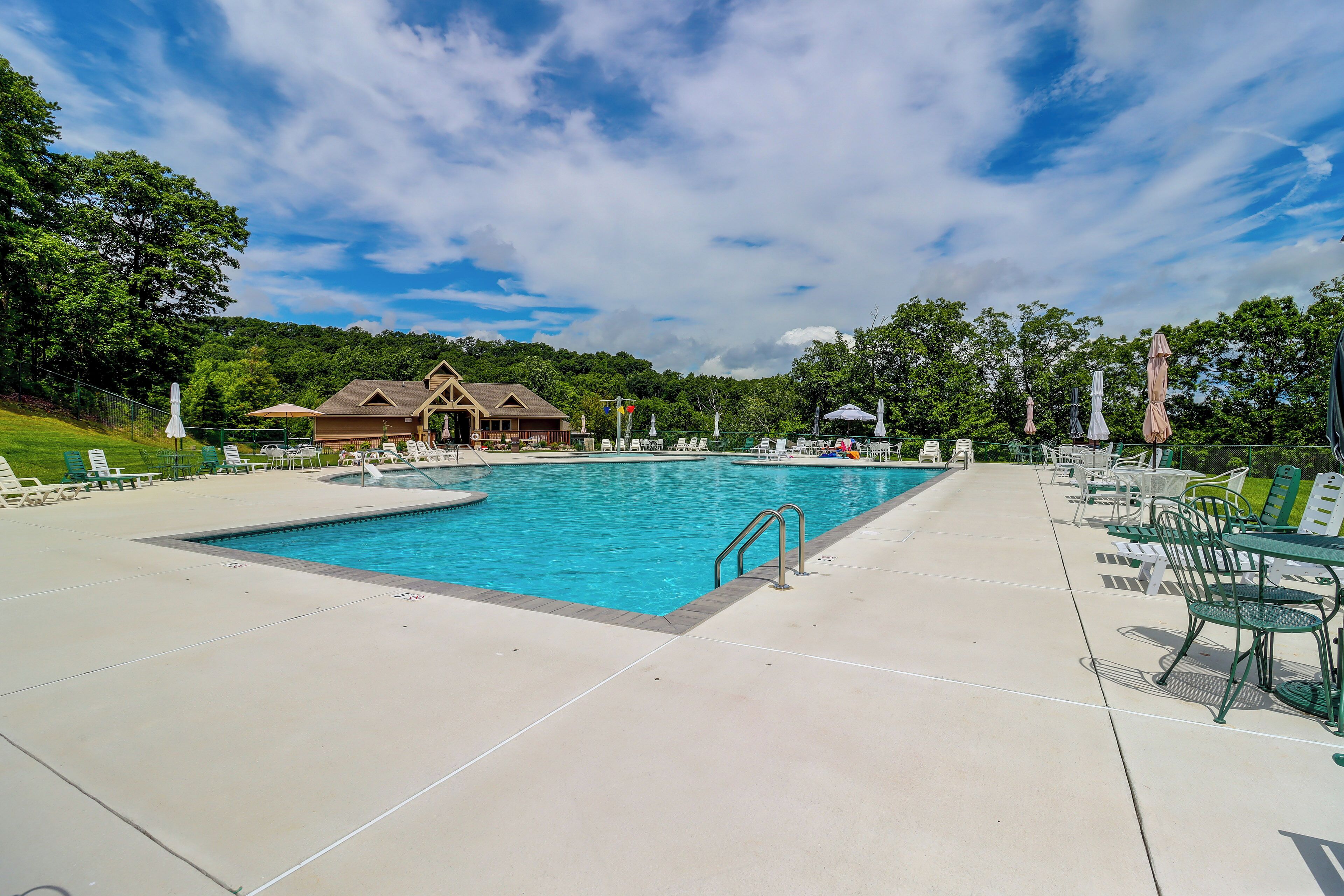 Ein Schwimmbecken mit Rettungsschwimmerstand, Liegestühlen und einem Gebäude im Hintergrund.