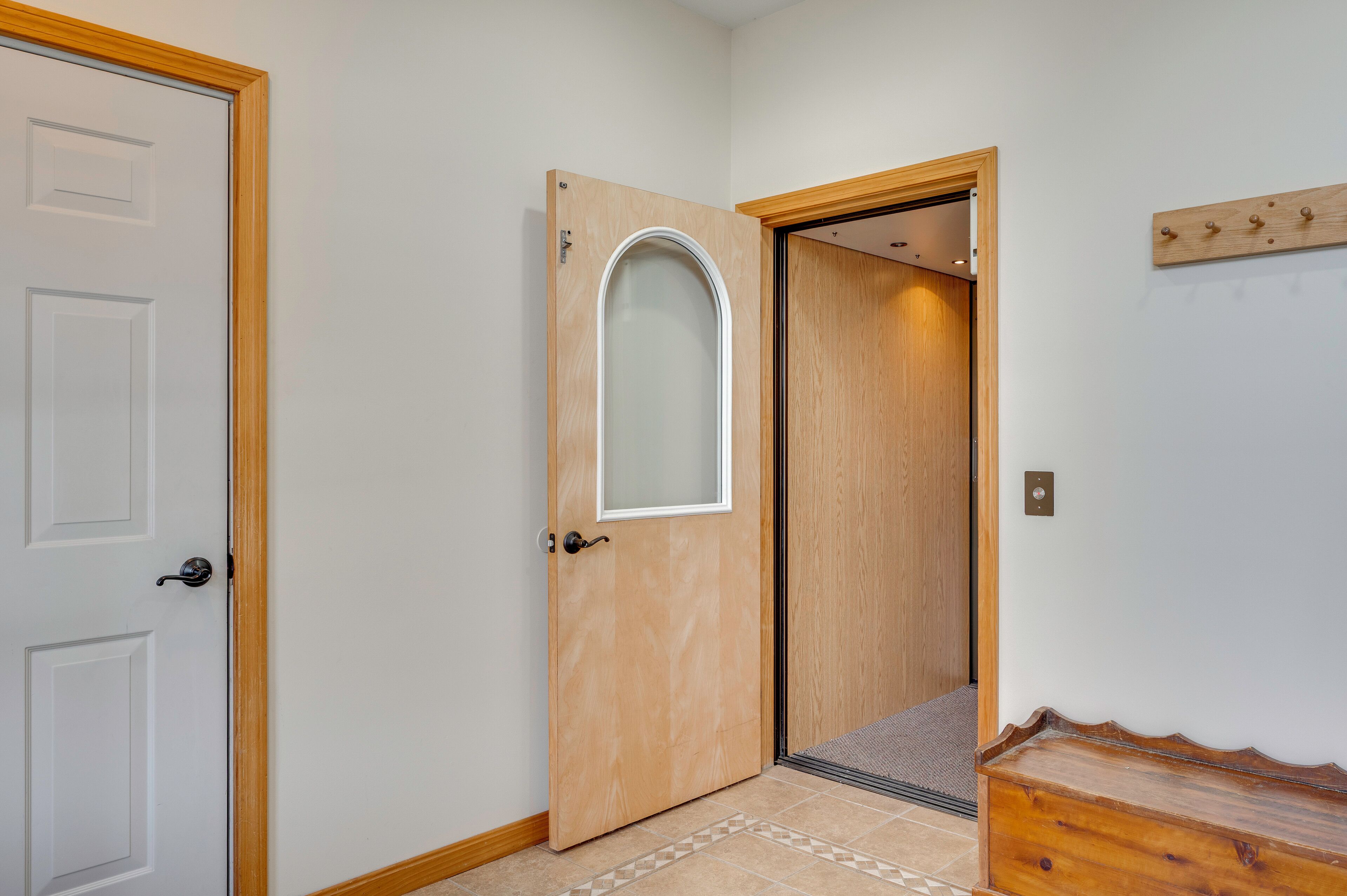 A hallway with a wooden door, a white door, and a wooden bench.