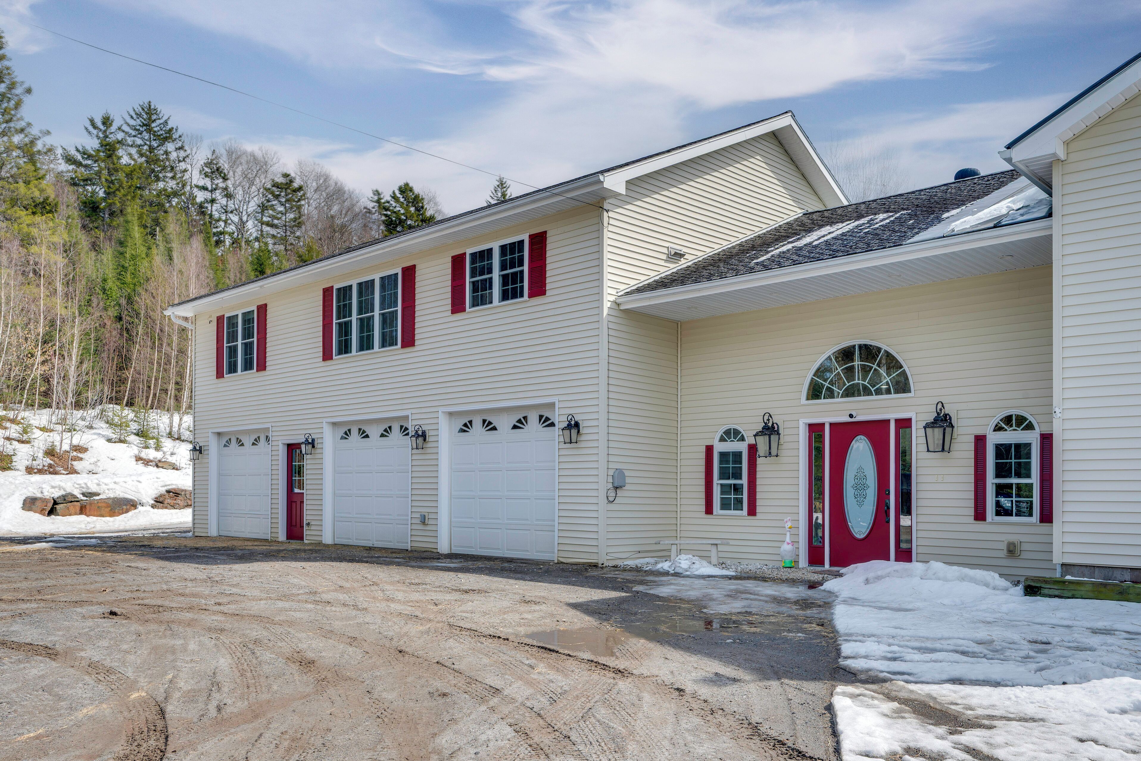 A two-story building with a garage, a red door, and a snow-covered ground.