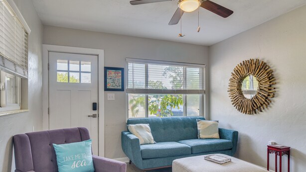 A living room with a blue sofa, a purple armchair, a ceiling fan, and a decorative mirror. - Private Yard & Patio! Tampa Bay Family Getaway (Pinellas Park)