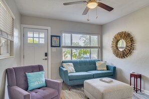 Una sala de estar con un sofá azul, un sillón púrpura, un ventilador de techo y un espejo decorativo.