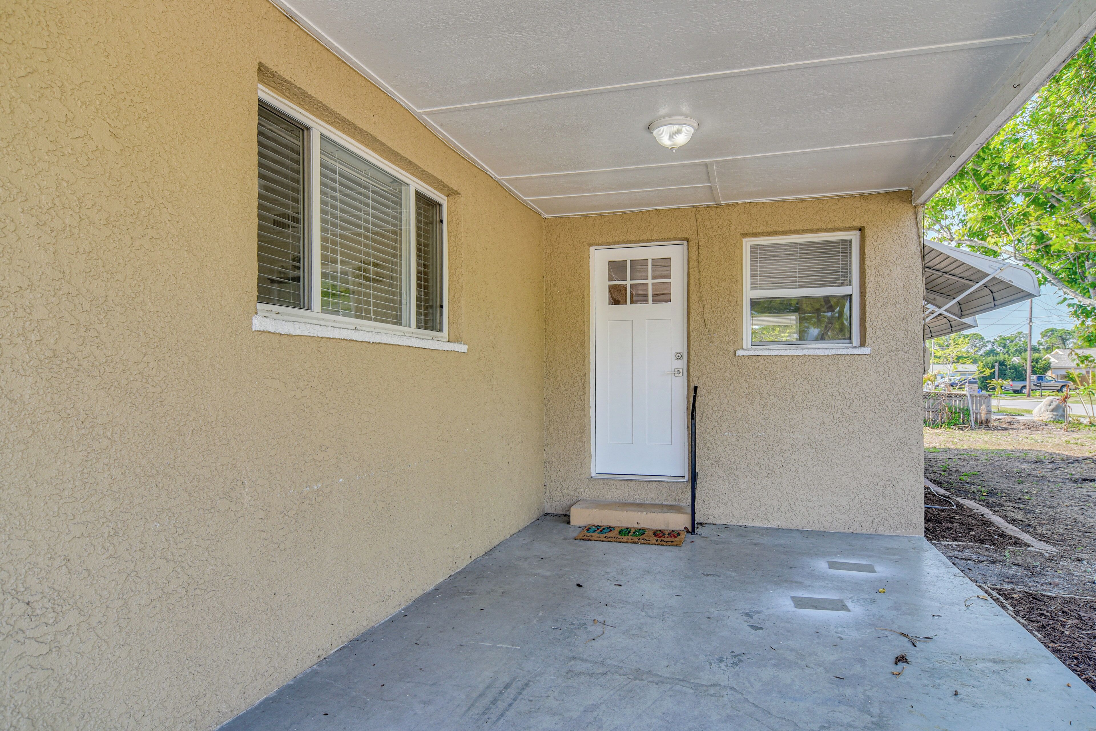 A house with a beige exterior, a white door, and two windows with blinds.