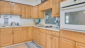 A kitchen with wooden cabinets, a white countertop, a stove, and a tiled backsplash. - Private Yard & Patio! Tampa Bay Family Getaway (Pinellas Park)