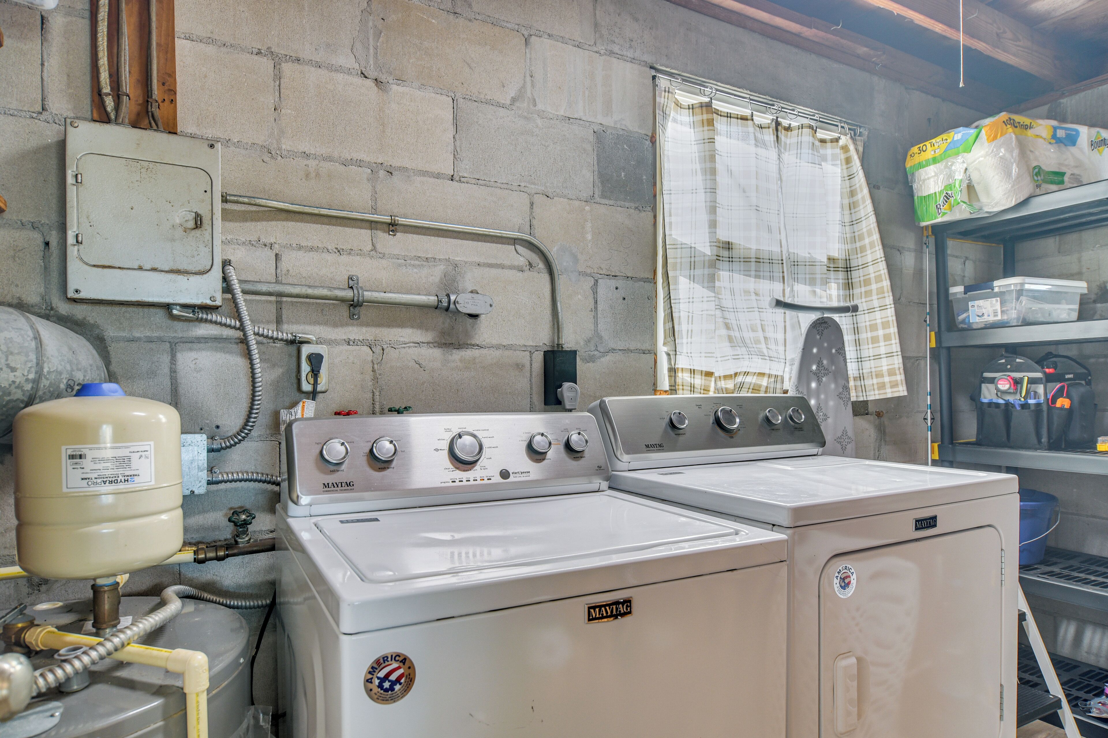 A laundry room with two Maytag washers and dryers, a water heater, and a utility cabinet with cleaning supplies.
