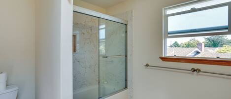 A bathroom with a glass-enclosed shower, a toilet, and a window with a view of the outside.