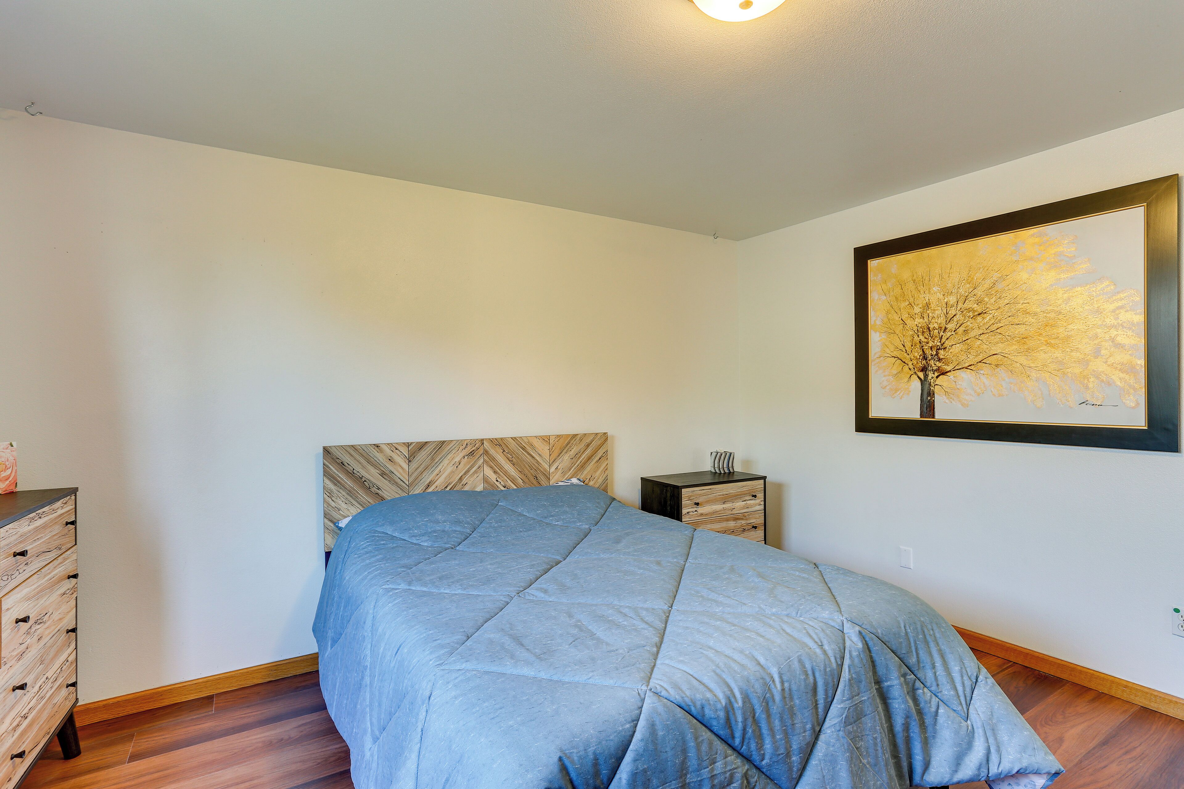 Un dormitorio con cama, cómoda, mesita de noche y un cuadro en la pared.