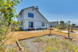 A two-story white house with a large front porch, a well-maintained garden with yellow flowers, and a clear blue sky.