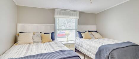 A bedroom with two beds, a ceiling fan, a window with blinds, and a nightstand with a lamp.
