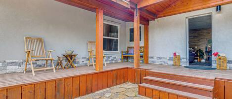 A covered outdoor deck with wooden furniture, stone flooring, and a view into the house.