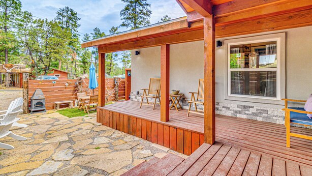 A wooden deck with outdoor seating, a stone patio, and a view of a forested area.
